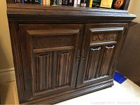 Front view of dark brown solid wood cabinet featuring two doors with carved panels and decorative scrollwork