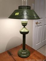 Green metal toleware table lamp full view showing the base, column, shade with perforated top and laurel wreath decoration.