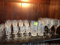 Shelf displaying over 30 crystal stemware pieces including tall wine glasses, goblets, and tumblers with cut star and fan patterns.