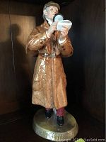 Front view of Royal Doulton 'The Detective' porcelain figurine in tan coat and hat holding magnifying glass and notepad.