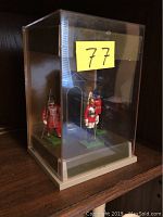 Front view of display case showing three Britains toy soldier figures standing on green bases inside a clear plastic case with a cream base.