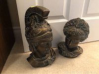 Pair of Romanesque busts with detailed helmet and hair styling, displayed on flat surface before white door.