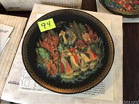 Top view of plate showing detailed painted scene with gold edge decoration and number sticker.