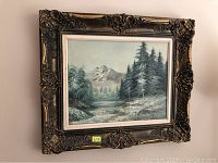 Full view of framed landscape painting showing snowy mountains, pine trees, and river scene.