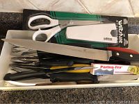 Overview of a tray containing over 30 kitchen knives and accessories including a large chef's knife, kitchen scissors, and boxed paring knife.