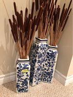 Front view of three blue and white rectangular vases filled with brown cattail decor, placed on carpeted floor against wall.
