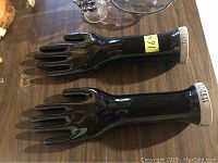 Two black glove moulds shaped like hands with detailed fingers, about 14 inches long, on a wooden surface.