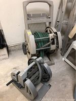 Green garden hose wound on a wheeled beige hose reel cart along with two other empty hose reels on floor.