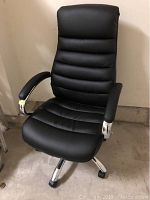 Front view of black office chair showing padded seat and backrest, padded armrests, and chrome base with caster wheels.