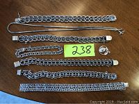 Overhead shot of eight sterling silver jewelry pieces arranged horizontally on a wooden surface with lot number card.