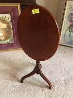 Front view of the oval wooden tilt-top table in vertical tilt position, showing the smooth wood finish and tripod base.