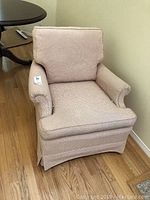 Front angle view of the beige upholstered side chair with arms and removable back cushion, showing overall shape and fabric condition.