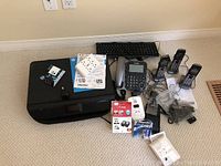 Photo showing HP Envy 4520 printer with paperwork on top, four Panasonic cordless phones with charging cradles, wired keyboard, and assorted cables and accessories