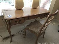 Full view of wood desk with three drawers and wood chair with wicker seat, showing top and legs