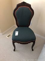 Front view of the small wood side chair showing carved top and upholstered green fabric seat and back with orange trim.
