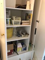 Shelf with assorted small items: plastic baskets, hand tools, papers, and cleaning/laundry bins