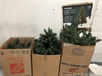 Photo shows three cardboard boxes containing disassembled artificial Christmas tree branches, including a Home Depot box.