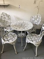 Photo of full bistro set with one round table and four matching white metal chairs, all featuring ivy leaf cutout designs.