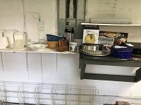 Photo showing various kitchen items on a shelf, including white ceramic canisters, mixing bowls, metal tins, glass pitcher in box, crepe pan, and some wooden utensils.