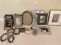 Overall view of collection showing multiple small frames in different colors and materials, including wood and metal, as well as pictures and decorative tiles among them.
