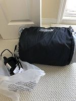 Rolled Coleman mattress inside black storage bag with branding, along with product tags and a plastic bag.