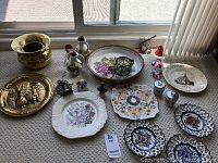 Wide view of all items arranged on carpet near window including decorative plates, brass plates, brass bowl, and small figurines.