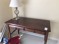 Dark wood desk shown from an angle with presence of two drawers and a metal lamp on top.