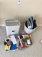 Overall view of the shredder with assorted file folders, binders and office supplies spread out on the floor and basket.