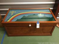 Front and top view of wooden hope chest showing painted lid with rainbow, mountains, cross and dove.
