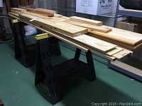 Full view of two black plastic sawhorses with assorted lumber pieces on top