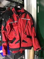 Red and black mens motorcycle jacket hanging, showing full front with adjustable straps and multiple pockets.