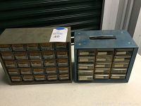 Two metal tool organizers side by side on table, showing drawer fronts and labels