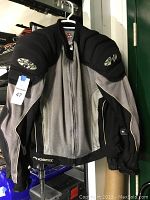 Front and hanging view of Joe Rocket Phoenix motorcycle jacket, showing grey and black mesh textile with piping and black padded shoulder protection with Joe Rocket logo.