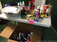 Wide view of cleaning supplies on table including sprays, polishes, gloves, sponges, and tape with plastic bins below.