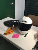 Full view of white HJC motorcycle helmet with dark visor installed and extra clear visor and storage bags on table
