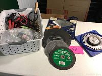 Lot overview showing plastic basket of assorted hand tools, several masonry cut-off wheels in front, and two saw blades to the right