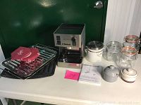 Full display on table of the Saeco Aroma coffee maker, assorted glass jars, ceramic containers, two broiler pans, and two Pampered Chef pan protectors.