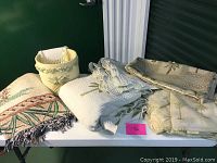 Overview of lot including cream-colored waste basket with palm leaf embossing, folded white quilt, throw blanket with palm leaf pattern edges, and folded palm print textiles.