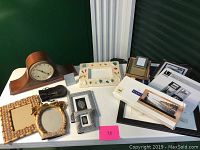 Full view of mantel clock with assortment of picture frames on a white table against green wall.