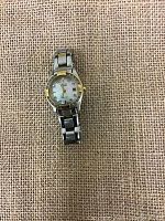 Citizen women's wristwatch on burlap background, showing the face and linked bracelet band.