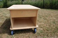 View of the work bench showing the open lower storage area and four blue caster wheels on the bottom.