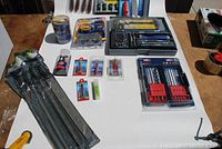 Overview of lot items spread on table including drill bits, socket set, and small hand tools mostly in packaging.