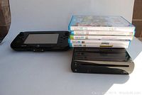 Black Nintendo Wii U console and GamePad controller next to stack of five Wii U game cases