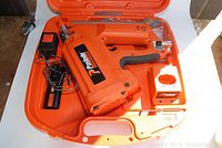 Open hard case showing nailer in foam-molded interior with charger, nails strip and oil bottle