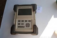 Front view of ANDO AQ-7155 mini-OTDR Protocol Analyzer showing screen and control buttons with rubber corner protectors.