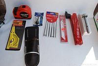 Black & Decker electric tape measure, angle finder, leather hammer holder, needle files, Sawzall blades, tool accessories arranged on surface.