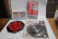 Overall lot showing the Freud power foot switch in box, two 10-inch saw blades (Freud and Bosch), the bench fabric vise packaging, and router bits.