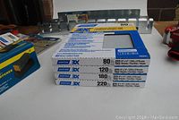 Photo showing stacked boxes of Norton 3X sandpaper sheets in 80, 120, 180, 220 grit sizes.