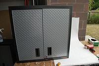 Front view of Gladiator garage cabinet with textured diamond plate metal double doors and locking key attached.