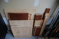 Various sized plywood panels and solid wood pieces stacked against wall including Russian birch plywood and walnut panels